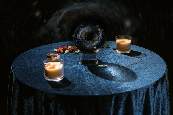 Kristallkugel in der Nähe von Kerzen und Wahrsagersteinen auf dunkelblauem Velourtuch auf schwarz - Foto, Bild