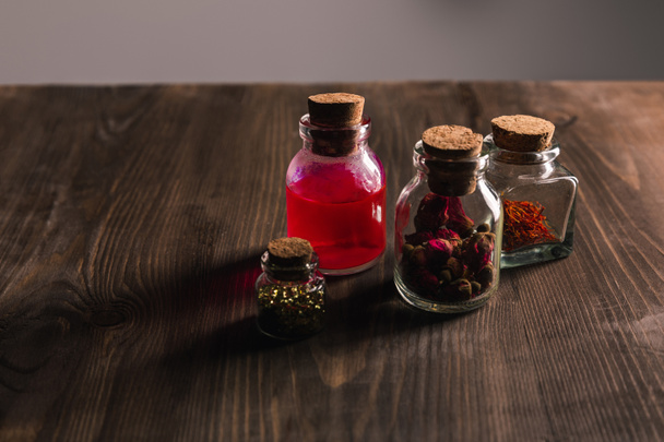 Üvegek rózsaszín rügyek, szárított gyógynövények és mágikus tinktúra fa és szürke háttér - Fotó, kép