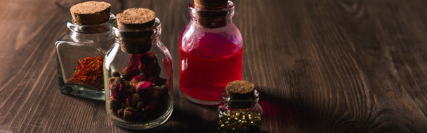 Jars with pink buds, dried herbs and magic tincture on wooden background, panoramic shot - Photo, Image