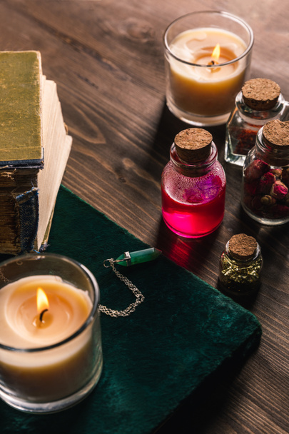 Jars with magic herbs and tincture, books and candles on wooden background - Foto, Imagen