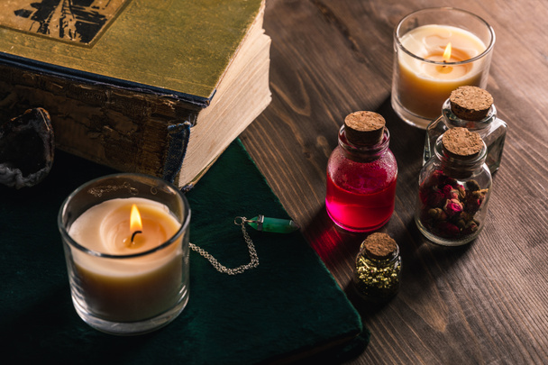 Frascos con hierbas mágicas y tintura, libros y velas sobre fondo de madera
 - Foto, imagen