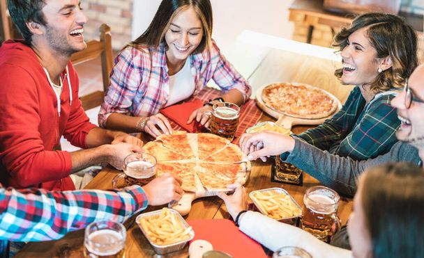 Young friends on genuine laugh while eating pizza at home on family reunion - Friendship concept with happy people enjoying time together having fun at pizzeria drinking brew pints - Warm vivid filter - Foto, imagen