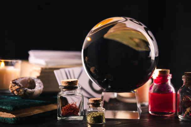 Selective focus of crystal ball with jars of dried herbs and tincture isolated on black - Foto, Imagem