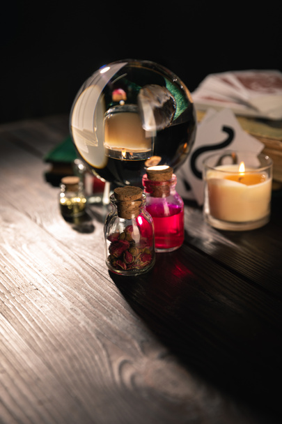 Selective focus of crystal ball, candle and jars of dried herbs and tincture isolated on black  - Photo, Image