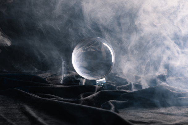 Bola de cristal sobre textil negro con humo sobre oscuro
  - Foto, Imagen