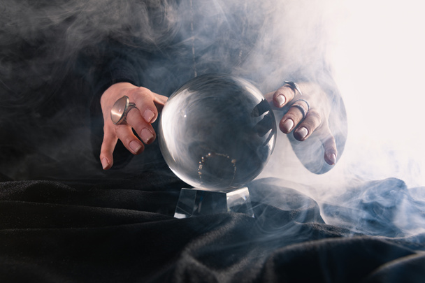 Osittainen näkymä naisten kädet lähellä kristalli pallo tummalla pohjalla
 - Valokuva, kuva