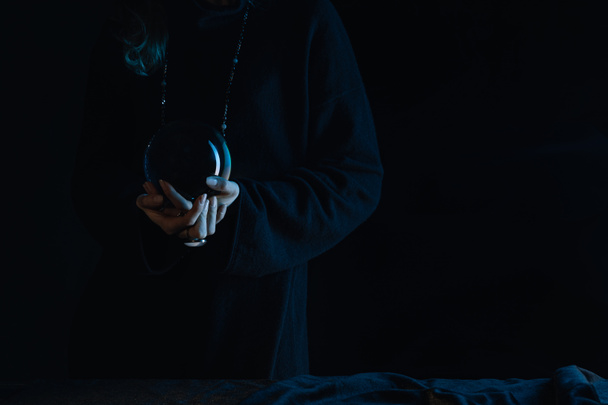 Siyah arka planda kristal küre tutan elleri sımsıkı bağlı cadının kırpılmış görüntüsü - Fotoğraf, Görsel
