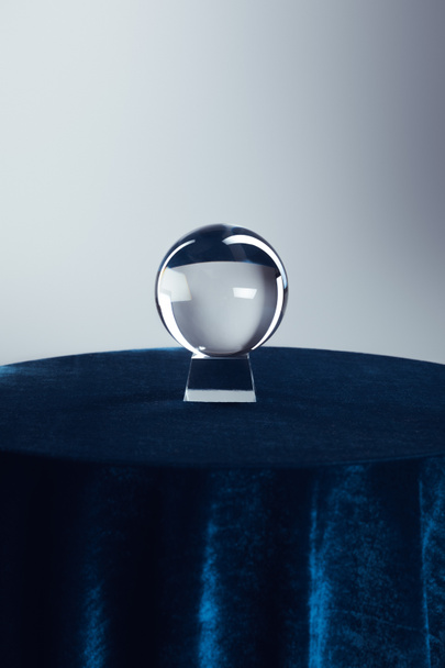 Křišťálová koule na kulatém stole s tmavě modrým ubrusem na šedém pozadí - Fotografie, Obrázek