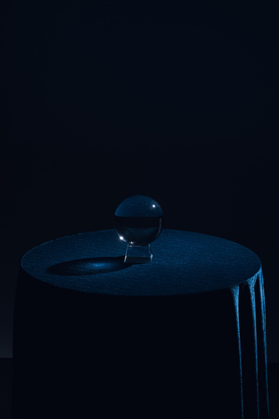 Sfera di cristallo su tavolo rotondo con tovaglia blu scuro su sfondo nero
 - Foto, immagini