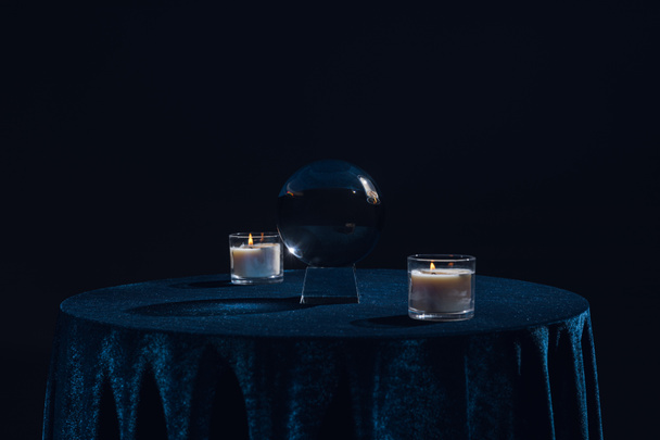 Crystal ball with candles on table isolated on black - 写真・画像