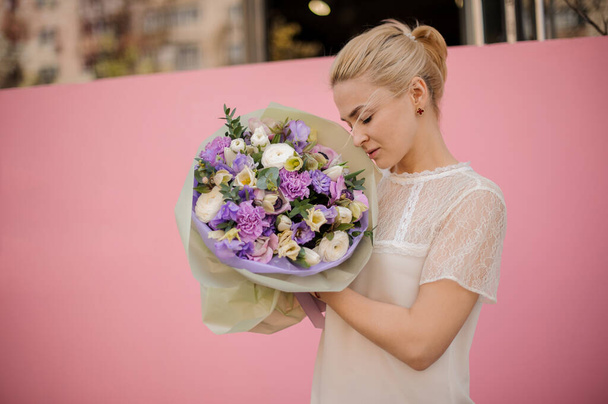 Girl holding a spring bouquet of tender violet and white color different flowers with leaves in a purple paper - Foto, Imagen