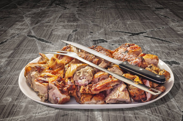 Φρεσκοψημένο χοιρινό κρέας, με σκαλιστό μαχαίρι και πιρούνι σερβιρίσματος, σερβίρεται σε μακρόστενο δίσκο πορσελάνης, σε παλιό φόντο ραγισμένο νιφάδα Pinewood τραπέζι πικ-νικ βινιέτα. - Φωτογραφία, εικόνα