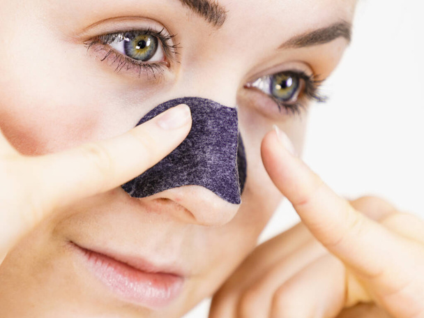 Woman appying clear-up strips on nose, using pore cleansing textile mask, on white. Girl taking care of skin complexion. Beauty treatment. Skincare. - 写真・画像