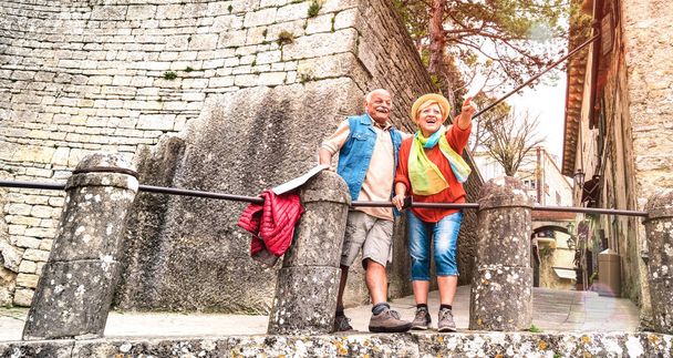 Senior retired couple having genuine fun in San Marino old town castle - Active elderly and travel lifestyle concept with mature people at italian roadtrip - Warm bright filter with soft sunshine halo - Photo, Image