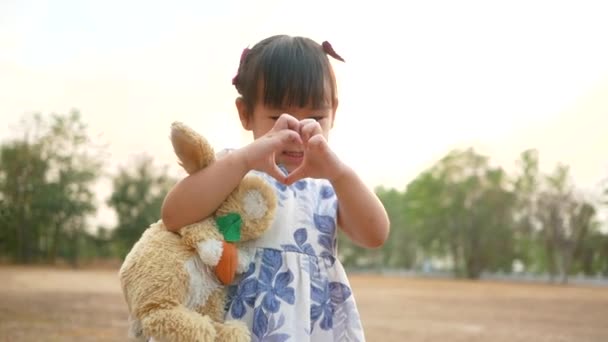 Cute Asian little girl hugging rabbit doll with smiley face in public park. - Footage, Video