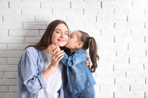 Young mother and little daughter near white brick wall. Space for text - Photo, Image
