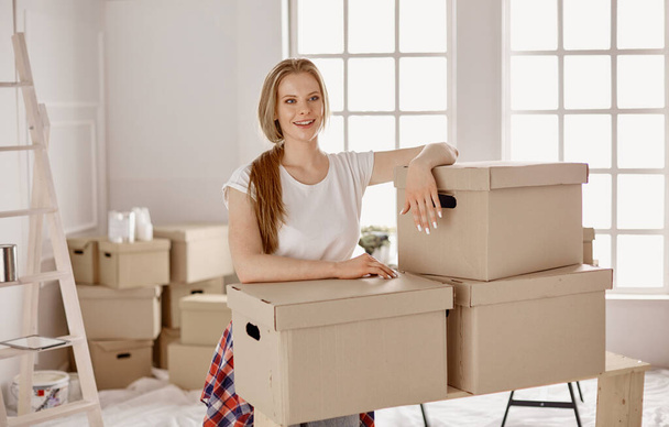 Kaunis yksittäinen nuori nainen purkamassa laatikoita ja muuttamassa uuteen kotiin - Valokuva, kuva