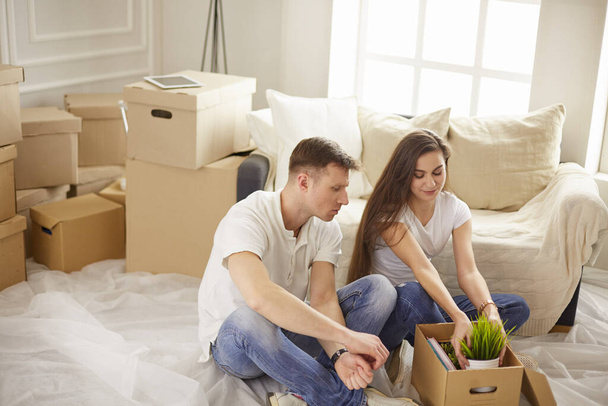 Portrait of happy couple looking at laptop computer together sitting in new house, surrounded with boxes - 写真・画像