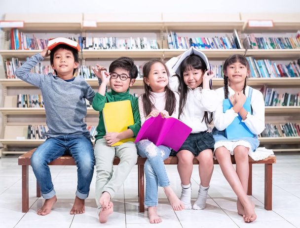Pět dětí sedí na dřevěné židli, v rukou drží knihu, připravují se ke studiu, s pocitem radosti a radosti, ve třídě, rozmazané světlo kolem - Fotografie, Obrázek