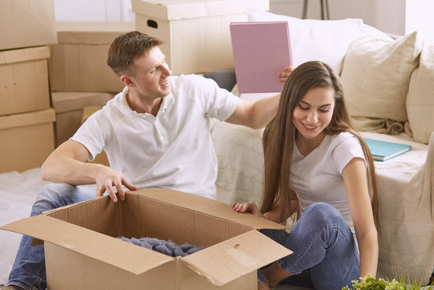 Portrait eines glücklichen Paares, das zusammen auf einem Laptop sitzt und in einem neuen Haus sitzt, umgeben von Schachteln - Foto, Bild