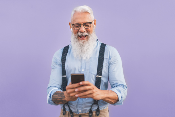 Homem sênior usando smartphone móvel e ouvir música com airpods - Homem maduro feliz se divertindo com novas tendências tecnologia aplicativos de mídia social - Pessoas idosas estilo de vida e conceito de vício em tecnologia
 - Foto, Imagem