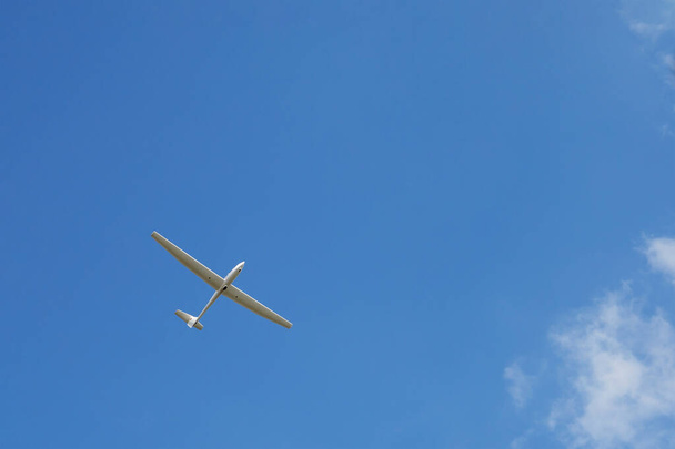 Спортивний планер у чистому блакитному небі. Синій фон неба з маленьким літаком для зображення свободи, польоту, нескінченних можливостей
. - Фото, зображення