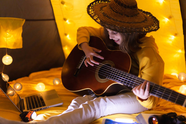 Little girl playing acoustic guitar under the tent in a living room. - Photo, Image