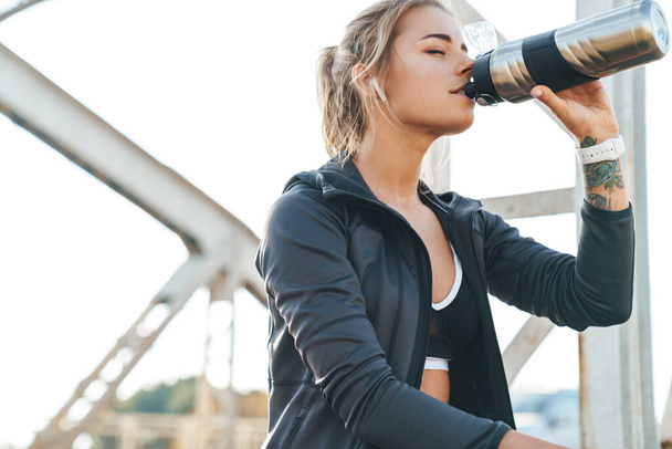 Photo of amazing beautiful young fitness woman sit outdoors drinking water. - Fotografie, Obrázek