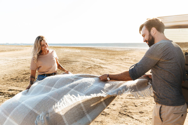 Image of a happy young amazing loving couple outdoors near car with mat litter at the beach. - Fotografie, Obrázek