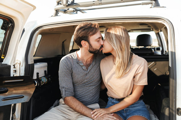 Image of a cute young amazing loving couple outdoors hugging in car at the beach kissing. - Photo, Image
