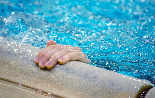 Una pequeña mano se extiende fuera de una piscina para agarrar el borde tal vez para evitar ahogarse
 - Foto, Imagen