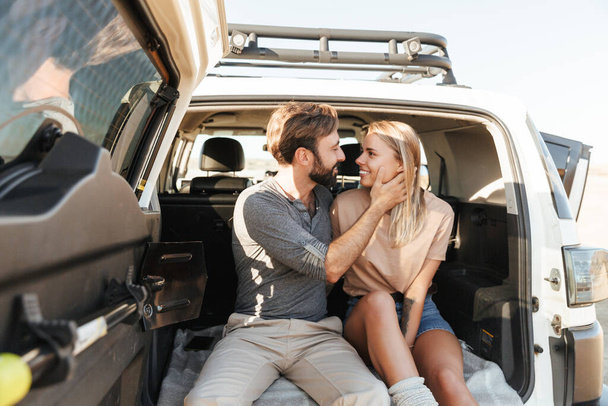 Image of a cute young amazing loving couple outdoors hugging in car at the beach. - Фото, изображение