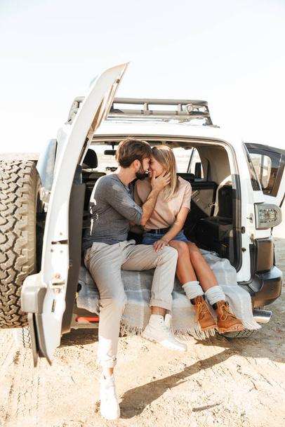 Image of a positive pleased happy young amazing loving couple outdoors hugging in car at the beach kissing. - Foto, afbeelding