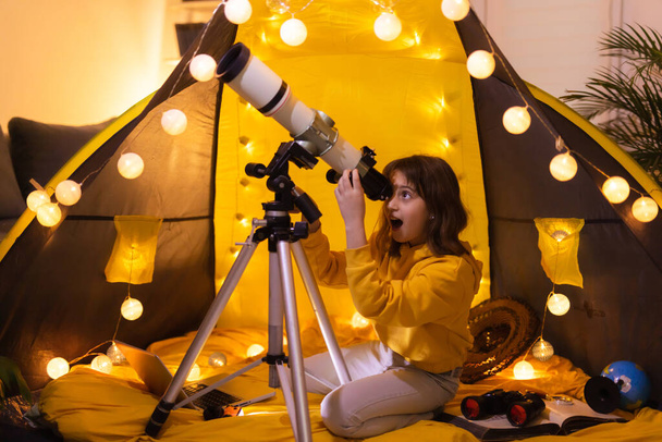 テントの中で自宅のリビングルームで望遠鏡を使用して小さな女の子. - 写真・画像