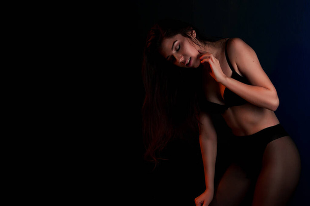 Cute young girl in black bra and pants wet skin stands posing leaning against the wall - Foto, afbeelding