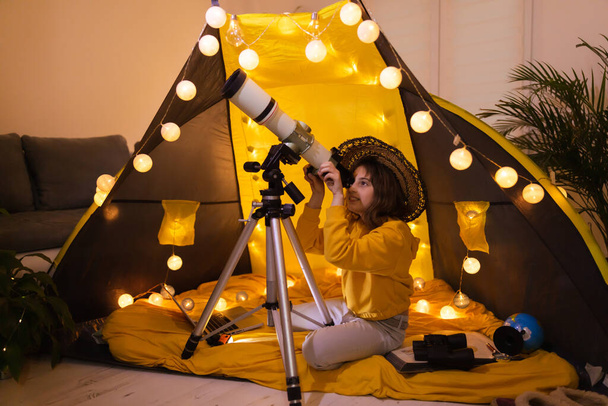 Small girl using telescope at home living room in a tent. - Foto, Imagem