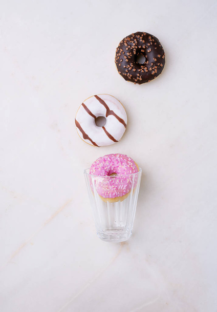 Glazed, chocolate frosted and sprinkled donuts with glass isolated on pink background. Top view - Photo, Image