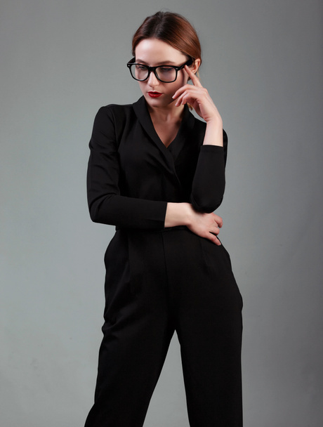 elegant business woman in black classic overalls and glasess posing over gray background. Happy satisfied relaxed elegant woman enjoy her work - Photo, image