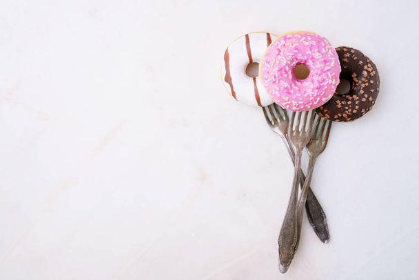 Glasiert, Schokolade gefrostet und bestreut Donuts auf Gabeln isoliert auf Marmor-Hintergrund. Ansicht von oben. Gabeln Wahnsinn eingestellt - Foto, Bild