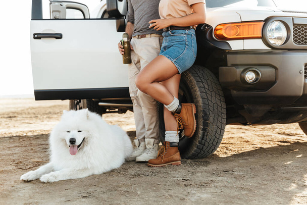Cropped photo of young loving couple with dog samoyed outdoors at beach near car. - Foto, Imagem