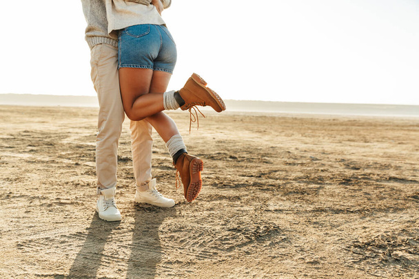 Cropped image of a young couple standing at the sunny beach, hugging - Foto, Imagen