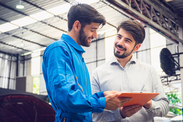 Mechanic holding clipboard with car owner in the workshop garage. Car auto services concepts - Foto, Bild