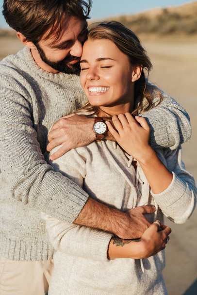 Fénykép fiatal elégedett mosolygós boldog szerető pár szabadban a strandon ölelés. - Fotó, kép