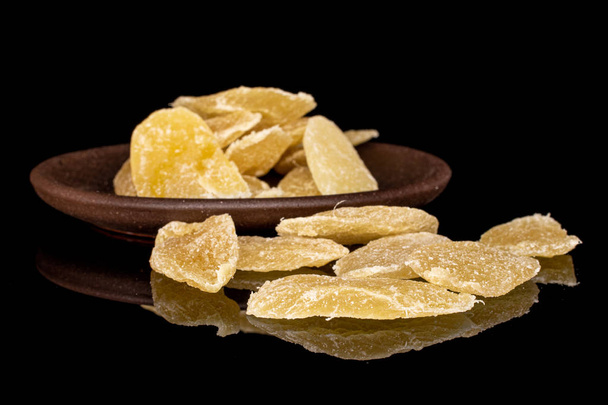 Lot of slices of sweet dried yellow pineapple with brown ceramic coaster isolated on black glass - Foto, immagini