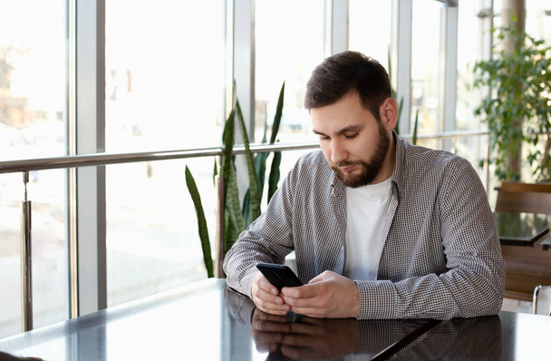 Phone conversation. Portrait smiling smart beard man in modern office with smartphone, texting messaging on application, check email, browsing internet web. Attractive businessman freelancer in cafe. - Photo, Image