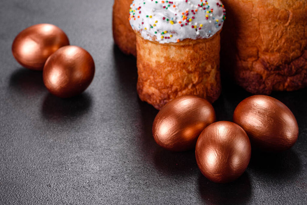 Huevos de Pascua de oro y bronce y pastel de Pascua sobre un fondo oscuro. Preparación para las vacaciones
 - Foto, Imagen