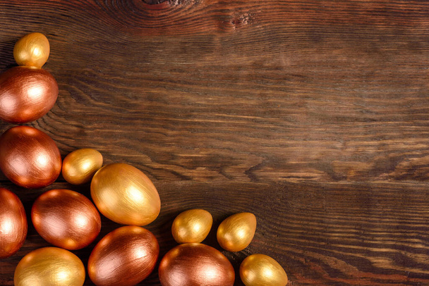 Huevos de Pascua de oro y bronce y pastel de Pascua sobre un fondo oscuro. Preparación para las vacaciones
 - Foto, Imagen