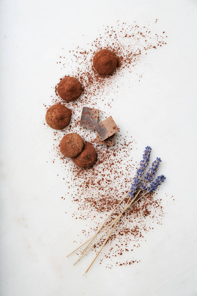 Pralinentrüffel, Schokoladenstücke und Lavendelstangen mit Kakaopulver über den Marmorhintergrund gestreut. Leckere Süßwaren-Kollektion. Ansicht von oben - Foto, Bild