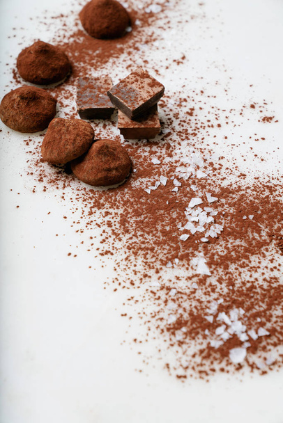 Pralinentrüffel und Schokoladenstücke mit Kakaopulver und Meersalz über den Marmorhintergrund gestreut. Leckere Süßwaren-Kollektion. Selektiver Fokus - Foto, Bild
