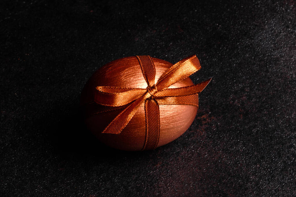 Ovo de Páscoa com fita de presente em um fundo de madeira escuro. Preparação para as férias
 - Foto, Imagem
